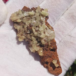 May include: A cluster of light green crystals on a brown, rough, rock-like matrix. The crystals are translucent and have a glassy luster.