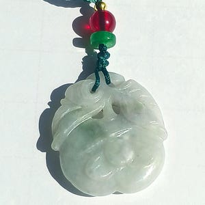 May include: A jade pendant carved in the shape of a fruit, with a green cord and red and green beads. The pendant has a light green and white color scheme, with detailed carving.