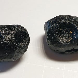 May include: Two black, irregularly shaped, volcanic rock specimens. The rocks have a rough, textured surface and appear to be porous.