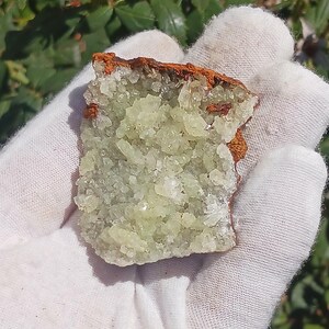 May include: A cluster of light green crystals with a brown, rough exterior. The crystals are clustered together in a dense formation, creating a unique and interesting texture.