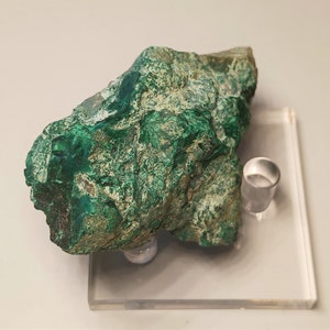 May include: A large, rough, green malachite specimen with a white matrix. The malachite is displayed on a clear acrylic stand.