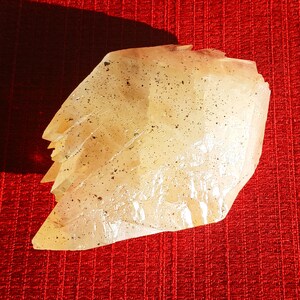 May include: A large, translucent, light yellow crystal with a rough, textured surface. The crystal has a pointed shape and is covered in small, dark specks.