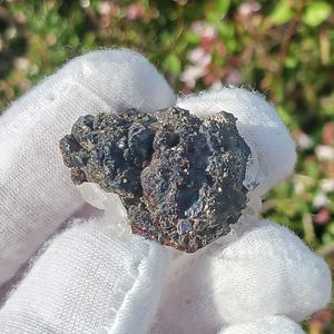 May include: A close-up of a dark grey and black mineral specimen with a rough, textured surface. The mineral is surrounded by white, crystalline material.