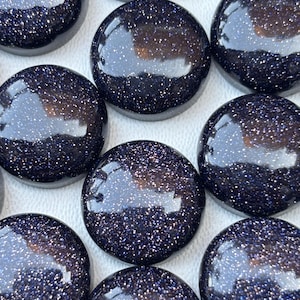 May include: Close-up of several polished, round, dark blue gemstones with sparkling inclusions. The stones have a smooth, reflective surface, and are arranged closely together. The gemstones are likely used for jewelry or decorative purposes.