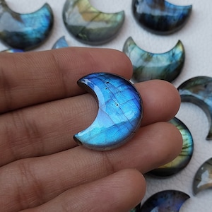 Pode incluir: Uma coleção de pedras de labradorita em forma de lua crescente. As pedras são de um azul profundo com reflexos iridescentes de verde e dourado.