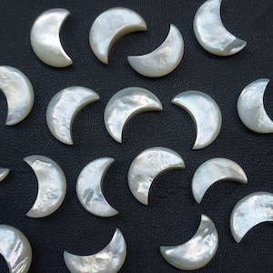 Può includere: Una collezione di pietre di madreperla bianche a forma di mezzaluna. Le pietre sono disposte in modo casuale su una superficie nera.