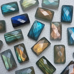 Puede incluir: Una colección de cabujones de labradorita en varios tonos de azul, verde y dorado. Las piedras están talladas en forma rectangular y tienen un acabado liso y pulido.