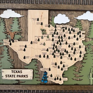 May include: Wooden Texas State Parks map with a brown frame. The map is light brown with dark green trees, white clouds, and a wooden sign that reads "Texas State Parks". A longhorn is also featured.