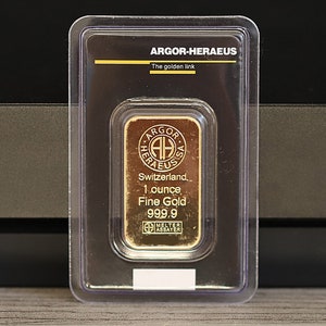 May include: A gold bar in a clear plastic case. The bar is labeled "Argor-Heraeus, The golden link, Switzerland, 1 ounce Fine Gold 999.9".