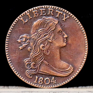 May include: A copper-colored 1804 Liberty Head coin with a portrait of a woman with flowing hair and the word "LIBERTY" above her head.