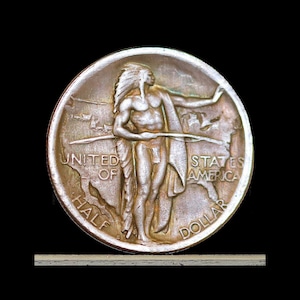 May include: A silver half dollar coin featuring a Native American figure with a feathered headdress, holding a bow. The coin is inscribed with "UNITED OF STATES AMERICA" and "HALF DOLLAR". The coin has a detailed relief design.