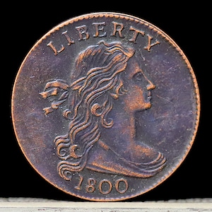 May include: A copper coin with the inscription "LIBERTY" and the year "1800" on it. The coin features a profile of a woman with flowing hair.