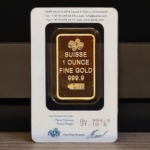 May include: A gold bar with the inscription "SUISSE 1 OUNCE FINE GOLD 999.9" in a clear plastic case. The bar is labeled with a certificate number, metal fineness, and metal weight. The certificate number is Au 999.9, the metal fineness is 31.10 g, and the certified assayer is "Kul".