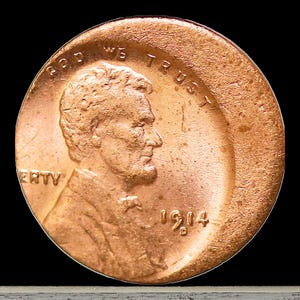May include: A close-up of a copper-colored 1914 Lincoln penny. The obverse side features a profile of Abraham Lincoln, the words "In God We Trust" and "Liberty". The year 1914 is visible.