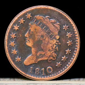May include: A copper-colored 1810 United States one-cent coin with a portrait of Liberty facing left and a circle of 13 stars around the portrait.