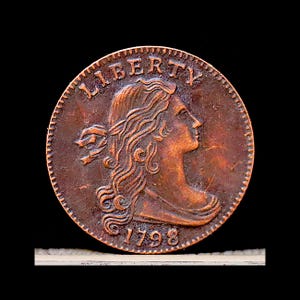 May include: A copper coin with a profile of a woman and the word "LIBERTY" at the top. The year "1798" is inscribed at the bottom. The coin has a detailed, aged appearance.