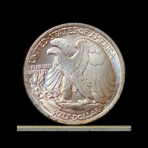 May include: A silver Half Dollar coin featuring an eagle with outstretched wings, the words "UNITED STATES OF AMERICA" and "HALF DOLLAR" are visible. The coin has a detailed design and is set against a black background.