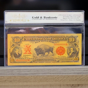 May include: A gold-plated $10 United States note with a buffalo and a portrait of a man. The note is encased in a clear plastic holder with a certificate of authenticity from Wishonor.