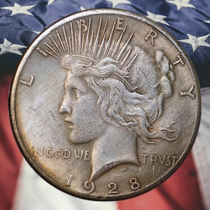 May include: A silver coin with a profile of a woman, the words "IN GOD WE TRUST" and the year "1928". The coin is set against a backdrop of the American flag, with red and white stripes and white stars.
