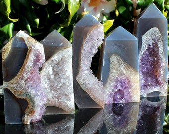 Peut inclure: Cinq pointes de cristal d'améthyste avec une finition druzy. Les pointes sont disposées en rangée, la plus grande à droite et la plus petite à gauche. Les pointes sont toutes de couleur violet clair et ont une texture naturelle et rugueuse. Les pointes se reflètent sur une surface brillante.