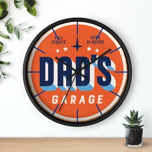 May include: A round, black-framed clock with a red, orange, and blue design. The clock face says "Dad's Garage" with the words "Full Service" and "Open 24 Hours" at the top.