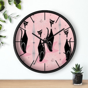 May include: A pink and black wall clock with a retro design featuring four black cats and silver stars. The clock has black hands and a black frame.