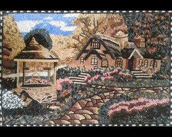 Puede incluir: Una obra de arte en mosaico que representa una cabaña pintoresca con techo de paja, rodeada de vegetación exuberante y un pozo de piedra con una tapa de madera. La escena se desarrolla sobre un fondo de cielo azul con nubes esponjosas.