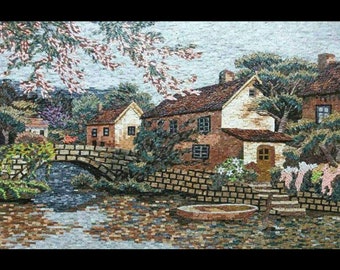 Puede incluir: Una obra de arte en mosaico que representa una pintoresca escena de pueblo con un puente de piedra sobre un río, dos casas con techos de tejas rojas y exuberantes árboles verdes. La obra de arte presenta una variedad de colores y texturas, creando una representación realista y encantadora de un entorno rural tranquilo.