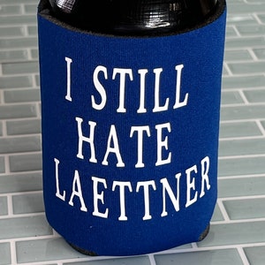 Puede incluir: Un enfriador de latas azul con el texto "I still hate Laettner" en blanco.