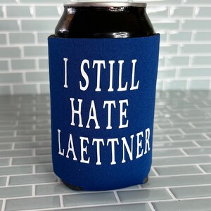 Puede incluir: Enfriador de latas azul con texto blanco que dice "I Still Hate Laettner".
