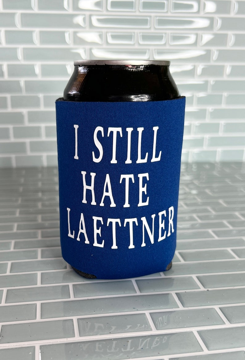 Puede incluir: Enfriador de latas azul con texto blanco que dice "I Still Hate Laettner".