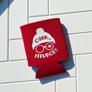 May include: A red beverage can cooler with a white graphic of a winter hat, glasses, and the phrase "OHHH... FFFUDGE!!" The cooler is made of a soft, insulating material.
