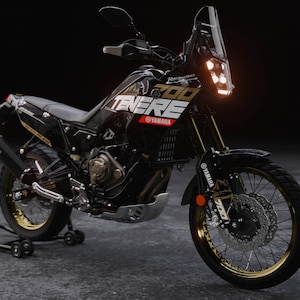 May include: Black and gold Yamaha Ténéré 700 motorcycle with the text "Ténéré 700" and "Yamaha" branding. The motorcycle has a black frame, gold rims, and a windshield. The motorcycle is parked on a gray surface.