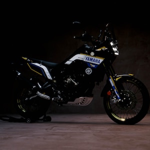 Può includere: Una moto Yamaha nera e blu con dettagli bianchi e gialli. La moto presenta il logo e il testo Yamaha. È parcheggiata su un supporto su uno sfondo scuro.