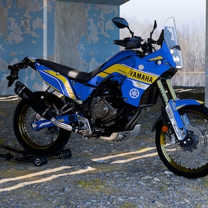 May include: A blue and yellow Yamaha motorcycle with the Yamaha logo prominently displayed. The motorcycle has a black exhaust pipe, gold-colored rims, and a clear windshield. The motorcycle is parked on a gravel surface.