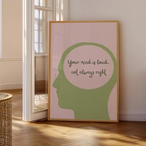 Könnte beinhalten: Ein gerahmter Kunstdruck mit hellrosa Hintergrund und einer grünen Kopfsilhouette. Im Inneren des Kopfes befindet sich ein grüner Kreis mit dem Text "Your mind is loud, not always right" in einer handschriftlichen Schriftart. Der Rahmen ist hellbraun.