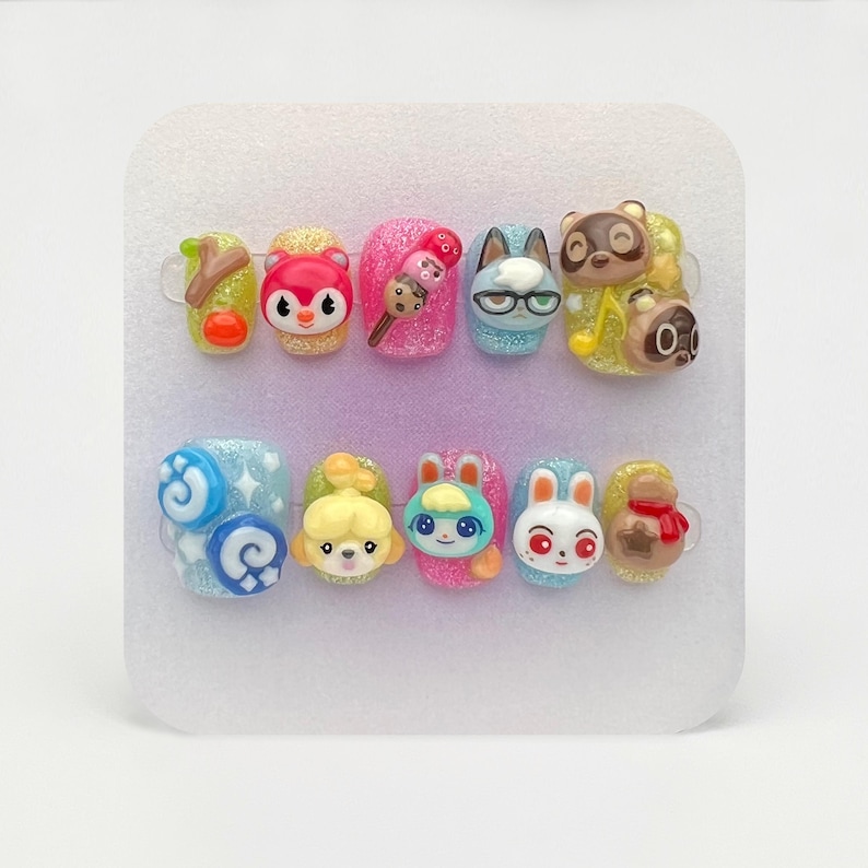 May include: A set of ten press-on nails with various character designs. The nails feature glitter, 3D embellishments, and cartoon characters in a variety of colors. The designs include a tree branch, a red squirrel, an ice cream cone, a cat with glasses, and a raccoon.
