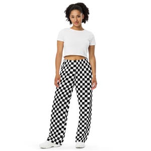 May include: A woman wearing a white crop top and black and white checkered wide-leg pants. The pants have a bold, repeating pattern of black and white squares. The outfit is completed with white sneakers.