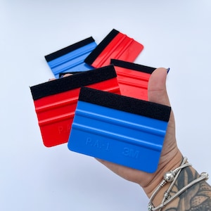 Puede incluir: Un juego de cuatro espátulas de aplicación de plástico azul y rojo con bordes de fieltro negro. Las espátulas tienen el logotipo de 3M y el texto "P.A.-1" impreso en ellas.