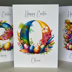 Um cartão colorido de Feliz Páscoa. Qualquer nome, cartão inicial. Cartão de Páscoa feito à mão com flores 3D, fita de arco-íris e pedras preciosas. Cartão de Páscoa personalizado