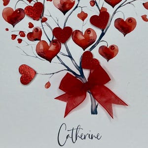 May include: A white card featuring a red watercolour tree adorned with red glitter hearts and a red bow. The name "Catherine" is inscribed at the bottom of the card.