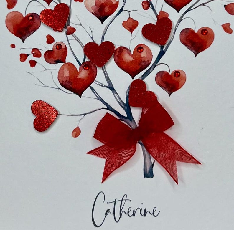May include: A white card featuring a red watercolour tree adorned with red glitter hearts and a red bow. The name "Catherine" is inscribed at the bottom of the card.