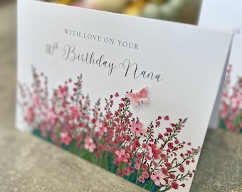 May include: A white card with pink flowers and a butterfly. The card says "With love on your 80th Birthday Nana".