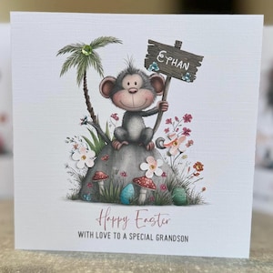 May include: Easter greeting card featuring a cartoon monkey holding a sign that reads "Ephan." The monkey sits on a rock surrounded by flowers, mushrooms, and an Easter egg. The card reads "Happy Easter with love to a special grandson."