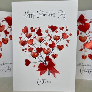 May include: A white card with the text "Happy Valentine's Day" and a red heart-shaped tree with a red bow. The name "Catherine" is written below the tree.