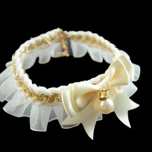 May include: A white lace choker with a gold trim and a large ivory satin bow with a pearl and rhinestone pendant.
