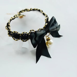 May include: A black choker necklace with a gold chain and a black satin bow with a pearl pendant.