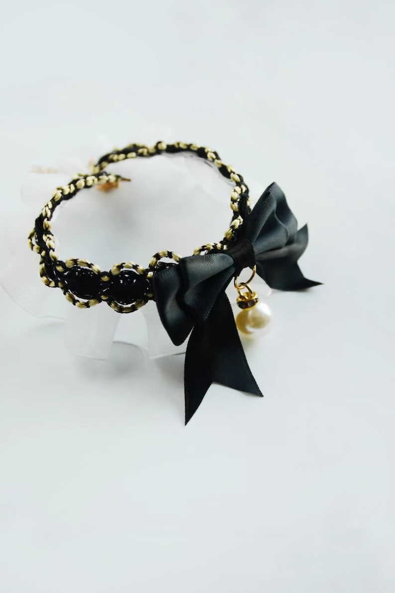 May include: A black choker necklace with a gold chain and a black satin bow with a pearl pendant.