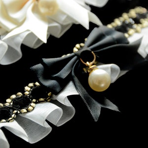 May include: Two white lace garters with bows and pearls. One garter has a black bow with a pearl pendant.