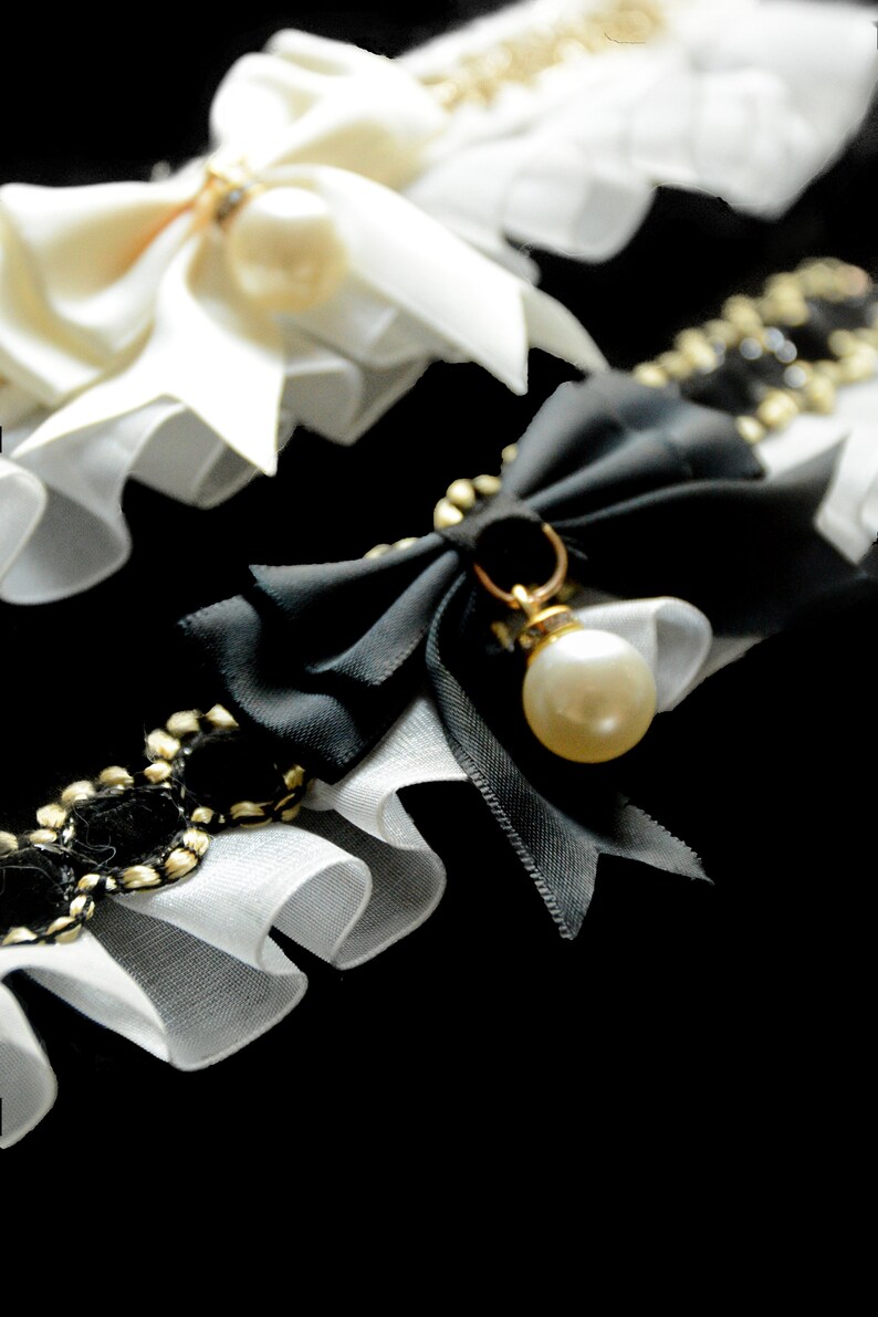 May include: Two white lace garters with bows and pearls. One garter has a black bow with a pearl pendant.